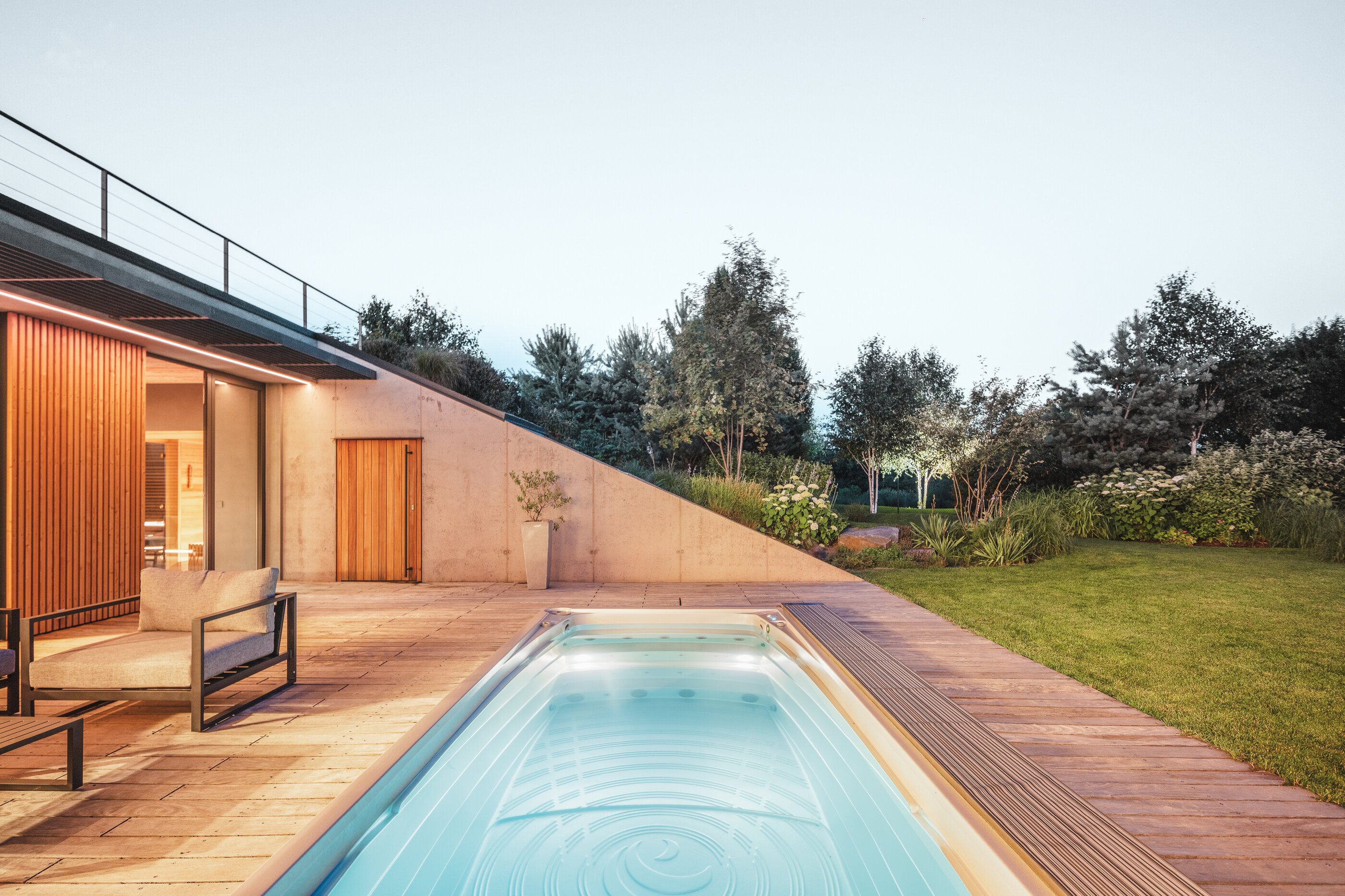 Swim Spa XL od USSPA integrovaná do dřevěné terasy, obklopená vzrostlou zahradou